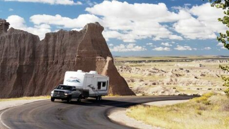 A truck-pulled RV drives down a road in the desert