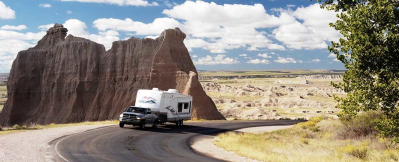 A truck-pulled RV drives down a road in the desert