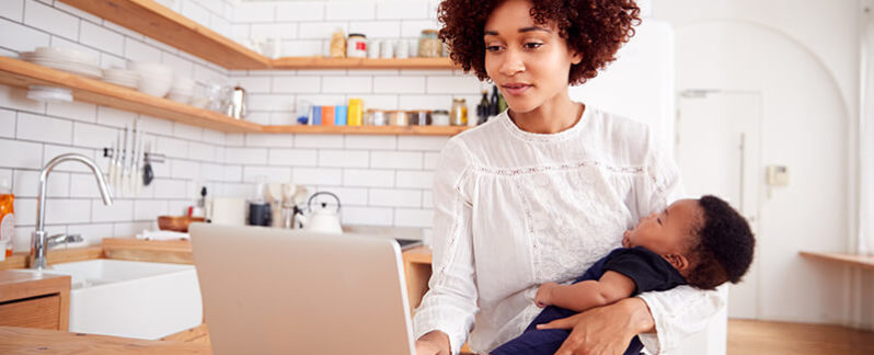 A mom uses her laptop to work while holding her baby