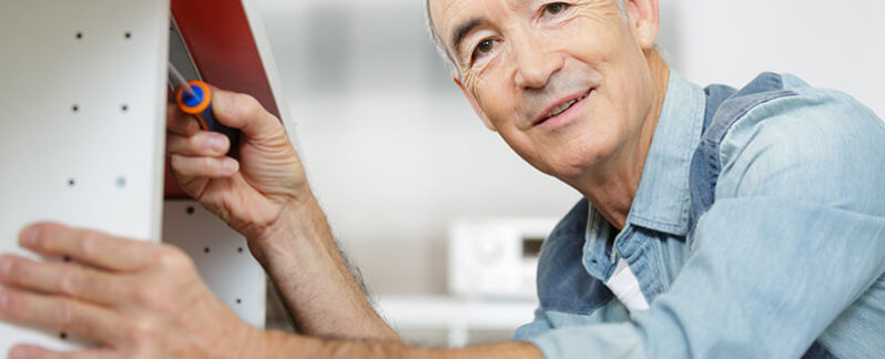 An older man attaches a screw to a shelf in their home