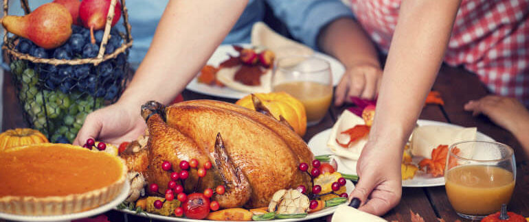 Person putting a baked turkey down on a table surrounded by people.