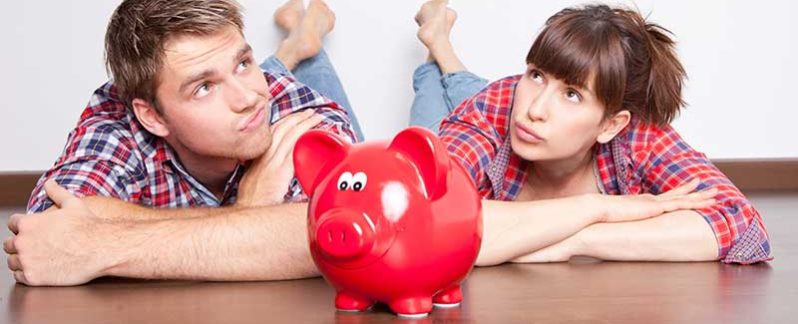 Couple sitting on the ground with a piggy bank in front of them.
