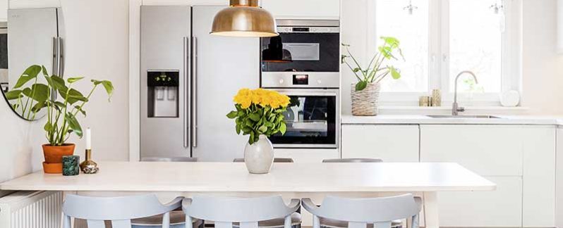 A pristine kitchen, with yellow flowers in a vase on the counter