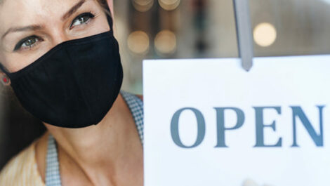 Woman with mask standing next to open sign.