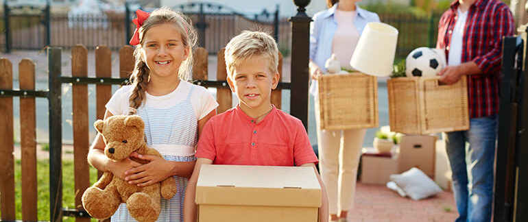 Two kids helping their parents move, holding boxes and toys.