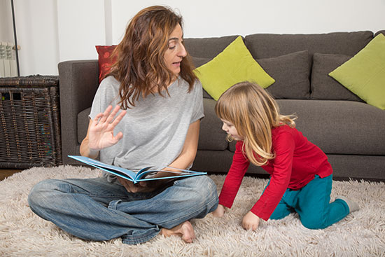 mom reading little girl a story about moving with kids on living room rug