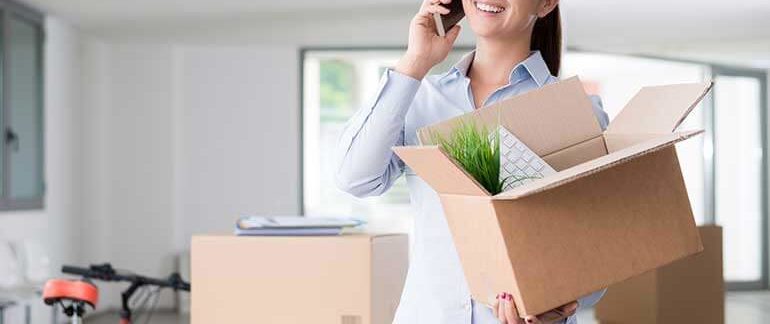 A woman talks on the phone while holding a box of her belongings.