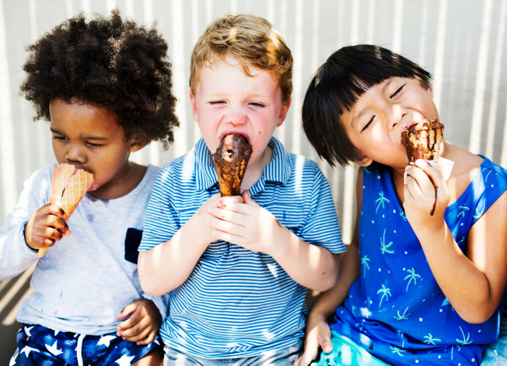 Children sitting down together eating ice cream.