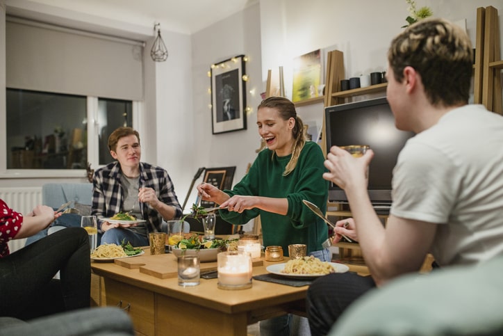 Four roommates gather around a table to share a meal.