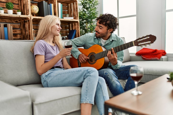 Man playing an acoustic guitar to a woman holding a wine glass.