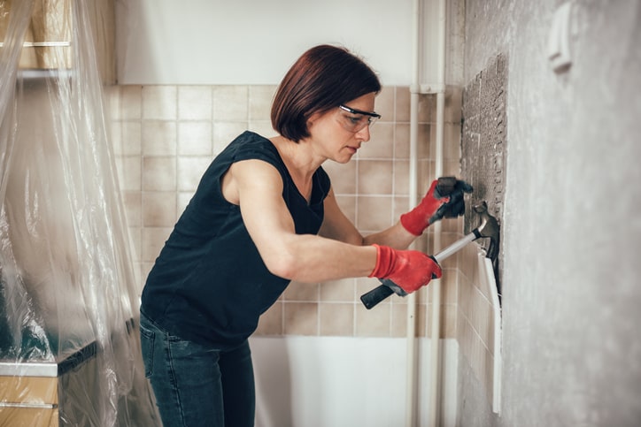 Woman pulling up bathroom tile with hammer. 