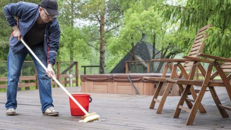 Man cleaning deck of summer home in front of covered in-ground hot tub.