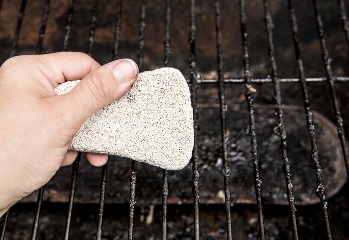 Man using grill stone to clean dirty grill grates.
