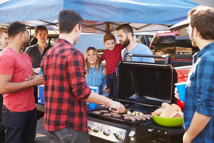Group of friends tailgating in stadium parking lot around a red truck.
