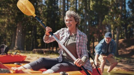 Smiling woman canoeing while partner pushes canoe into the water behind her.