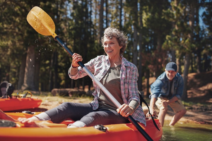 Smiling woman canoeing while partner pushes canoe into the water behind her.