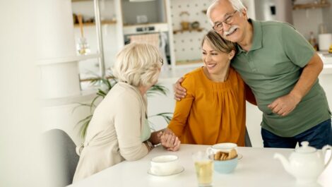 Aging parents hugging adult daughter at kitchen counter