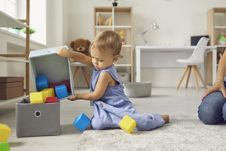 Toddler dumping toy blocks into a fabric bin