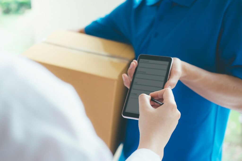 A woman uses a stylus to sign on a phone held by a delivery person holding a cardboard box