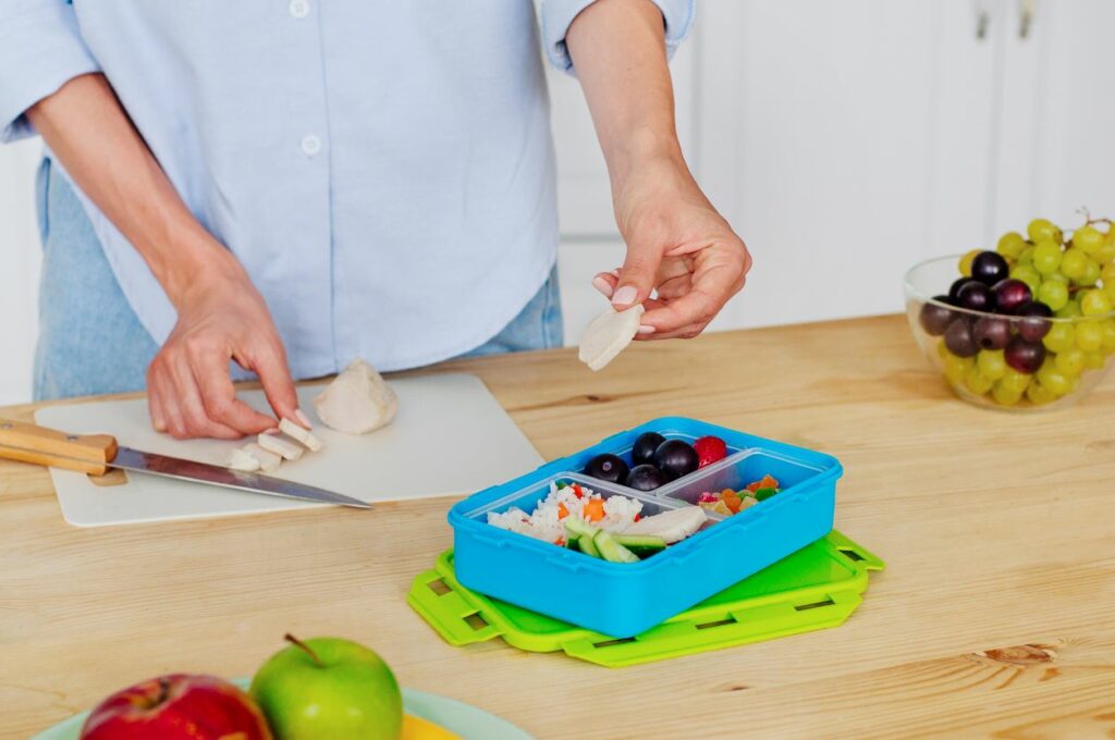 A woman preparing a healthy boxed lunch with fruit and chicken