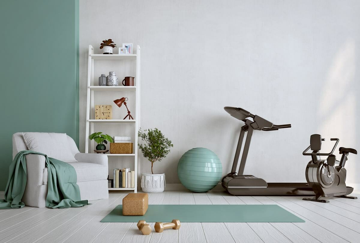 A home gym with a teal yoga mat, gold dumbbells, treadmill, exercise ball, and stationary bike