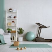 A home gym with a teal yoga mat, gold dumbbells, treadmill, exercise ball, and stationary bike
