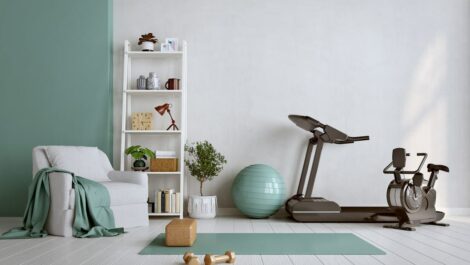 A home gym with a teal yoga mat, gold dumbbells, treadmill, exercise ball, and stationary bike