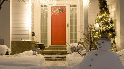 Icicle lights dangle on a porch with a snowman built in the yard