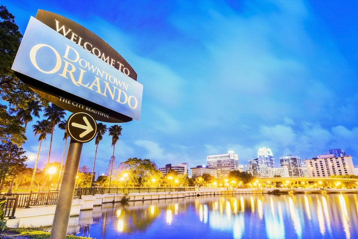 Downtown Orlando sign and city skyline at dusk with lights reflecting on the water.