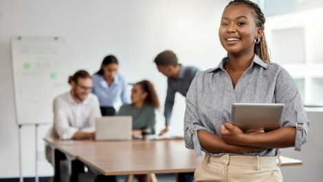 Young professional standing in a boardroom, with a tablet.