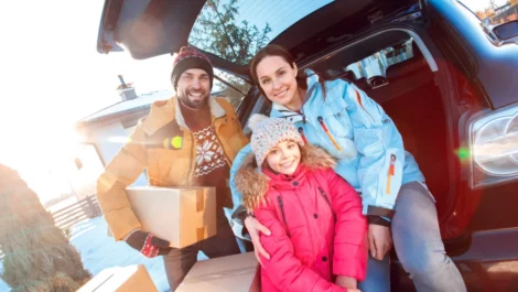 Family sitting on their car trunk holding boxes.