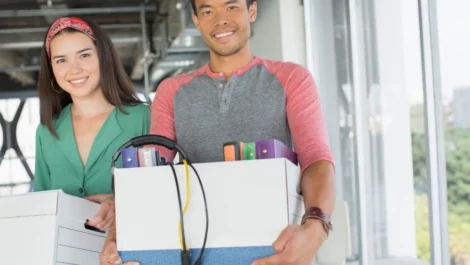 Employees carrying packed boxes full of headphones and binders through workspace.