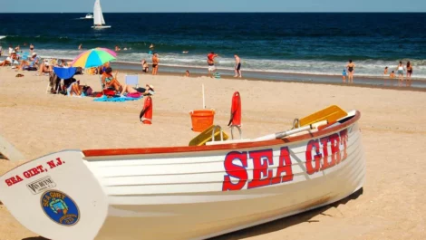 A white boat that reads "Sea Girt" sitting in the sand on a beach