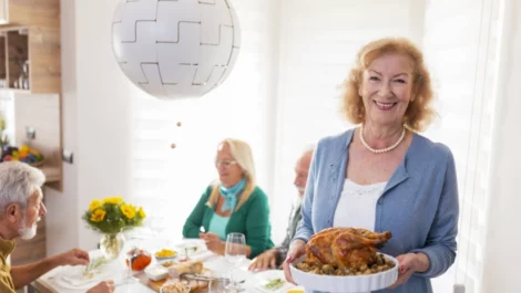 A senior woman smiles as she serves turkey to her family at a Thanksgiving dinner.