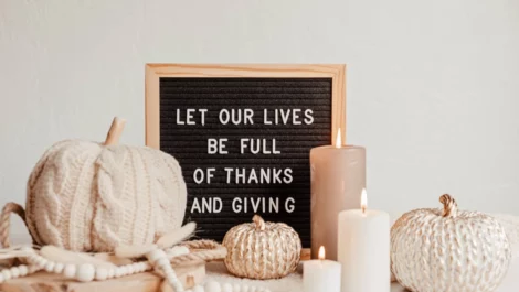 A letterboard sign reads "Let our lives be full of thanks and giving," surrounded by knitted pumpkins and candles.