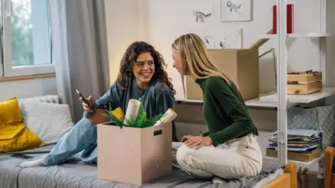 Two women sitting on a bed with a box