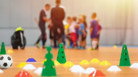 Soccer cones set up on the floor with a soccer team blurred in the background.